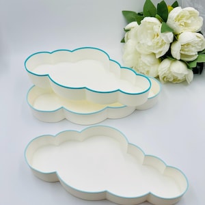 May include: Three white cloud-shaped trays with a teal blue rim. The trays are stacked on top of each other.