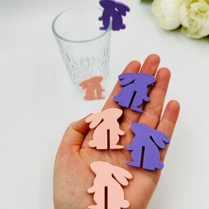 May include: Five bunny shaped drink markers in pink and purple. The markers are made of a soft material and are perfect for adding a touch of whimsy to your drinks.
