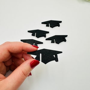 Könnte beinhalten: Schwarze Abschlusskappen-Ausschnitte. Eine wird von einer Hand mit rotem Nagellack gehalten. Vier weitere sind auf einer weißen Oberfläche verstreut. Die Kappen haben ein strukturiertes Aussehen und sind diagonal angeordnet.