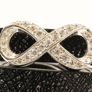 May include: A silver infinity charm with clear rhinestones set on a black leather bracelet.