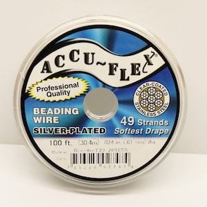 Könnte beinhalten: Eine Spule mit versilbertem Perlenfaden, beschriftet mit "ACCU-FLEC Professionelle Qualität Perlenfaden Versilbert 49 Litzen Weichster Fall 100 ft (30,4 m) 0,024 Zoll (6,1 mm) Durchmesser Hergestellt in Japan Nachbestellen 123 2691BS".