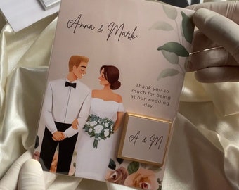 Könnte beinhalten: Eine Dankeskarte zur Hochzeit mit einer Cartoon-Illustration eines Brautpaares. Die Karte ist rosa mit grünen Blättern und weißen Blumen. Der Text auf der Karte lautet "Anna & Mark" und "Vielen Dank, dass Sie bei unserer Hochzeit dabei waren". Ein kleines goldenes Quadrat mit dem Text "A & M" ist an der Karte befestigt.
