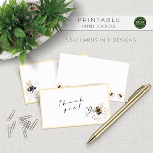May include: Printable mini cards with a bee and floral design. The cards are 3.5 x 2 inches and feature the text "Thank you!" with a heart. A gold pen and paper clips are also in the image.