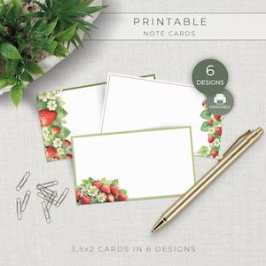 Peut inclure: Un ensemble de cartes de notes imprimables avec des illustrations de fraises, fleurs blanches et feuilles vertes. Le lot comprend 6 designs de 3,5x2 pouces. Un stylo doré et des trombones argentés sont disposés près des cartes.