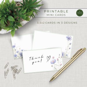 Puede incluir: Mini tarjetas imprimibles con un diseño floral. Las tarjetas son blancas con un borde verde claro y presentan flores azules y rosas de estilo acuarela. El texto "Thank you!" está escrito en una tarjeta. Un bolígrafo dorado y clips también están en la imagen.