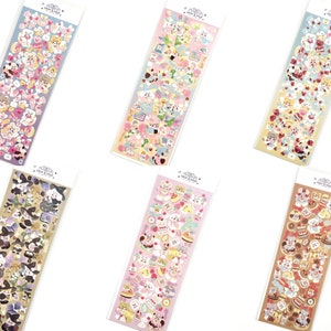 May include: Six sticker sheets with various designs. Each sheet is rectangular and filled with colorful, cartoon-style illustrations. The stickers feature themes like animals, food, and other cute elements. The sheets are packaged in clear plastic.