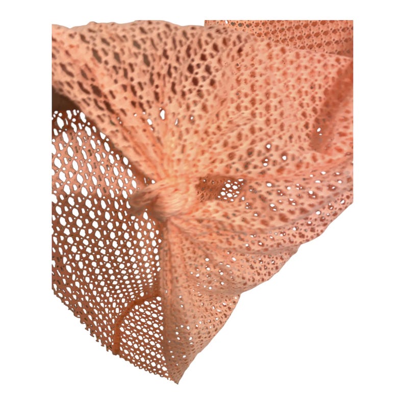 May include: A peach-colored fabric accessory featuring an open-knit, mesh-like texture. The material is gathered and secured with a central knot, creating a series of folds and drapes that highlight the intricate, repeating geometric pattern of the weave.