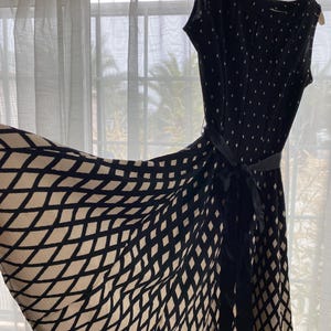 Puede incluir: Un vestido con estampado negro y beige con cinturón negro. El vestido tiene un diseño sin mangas y una falda fluida con un patrón de diamantes. La parte superior del vestido tiene un estampado de lunares.