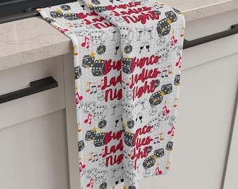 Peut inclure: Serviette de cuisine blanche avec un motif répété de dés, de notes de musique et le texte "Bunco Ladies Night".