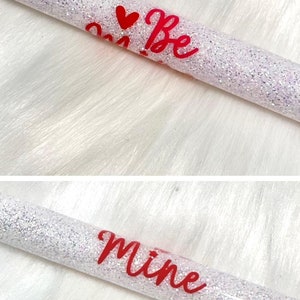 May include: White glitter tube with the words "Be Mine" in red cursive lettering and a red heart.