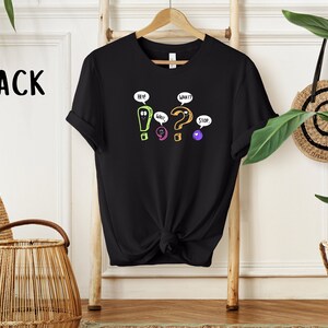 May include: Black t-shirt with a graphic of colorful punctuation marks with faces and speech bubbles. The speech bubbles say "Hey!" "What?" "Cool" and "Stop."