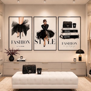 May include: Three framed wall art prints featuring fashion illustrations. The left print shows a high heel with a large black bow. The centre print depicts a person in a black dress. The right print displays a stack of books labelled Chanel, Prada, Vogue, and Tom Ford.