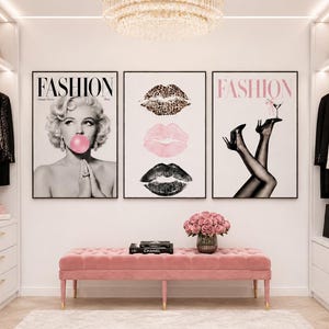 Op de afbeelding: Een set van drie ingelijste wandposters met een zwart-witportret van een vrouw die een roze kauwgombel blaast, drie verticaal geplaatste lippen in luipaardprint, roze en zwart, en een paar benen op hakken die een martiniglas vasthouden.