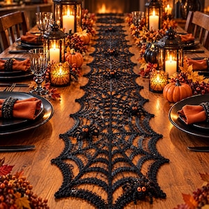 Peut inclure: Un chemin de table en dentelle noire avec un motif de toile d'araignée détaillé et plusieurs petites figurines d'araignées noires aux yeux orange, disposé sur une table à manger en bois avec des serviettes orange et des lanternes.