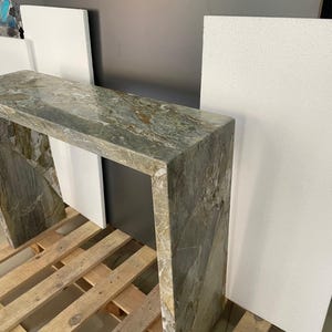 Pu&ograve; includere: Un tavolo consolle in marmo verde con un piano rettangolare e una struttura aperta. Il tavolo &egrave; appoggiato su un pallet di legno.