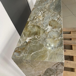 Pu&ograve; includere: Una grande lastra rettangolare di marmo verde e bianco con un motivo a spirale. La lastra &egrave; appoggiata su un pallet di legno.