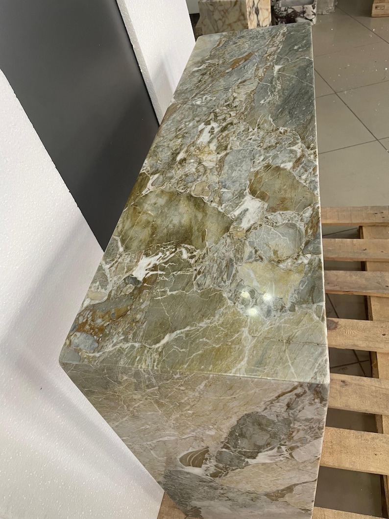 Pu&ograve; includere: Una grande lastra rettangolare di marmo verde e bianco con un motivo a spirale. La lastra &egrave; appoggiata su un pallet di legno.