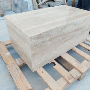 Op de afbeelding: Een grote, rechthoekige, lichtbeige travertijnstenen blok, liggend op een houten pallet. De steen heeft een natuurlijk, geaderd patroon.