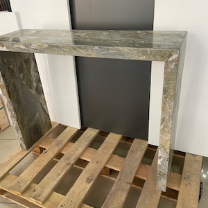 Pu&ograve; includere: Un tavolo consolle in marmo verde con piano rettangolare e base quadrata. Il tavolo &egrave; in pietra naturale e ha una finitura lucida.