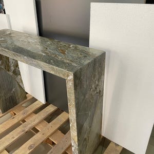 Pu&ograve; includere: Un tavolo console contemporaneo realizzato in marmo verde con un design asimmetrico unico. Il tavolo &egrave; sostenuto da un'unica gamba spessa su ogni lato, creando un look moderno e minimalista.