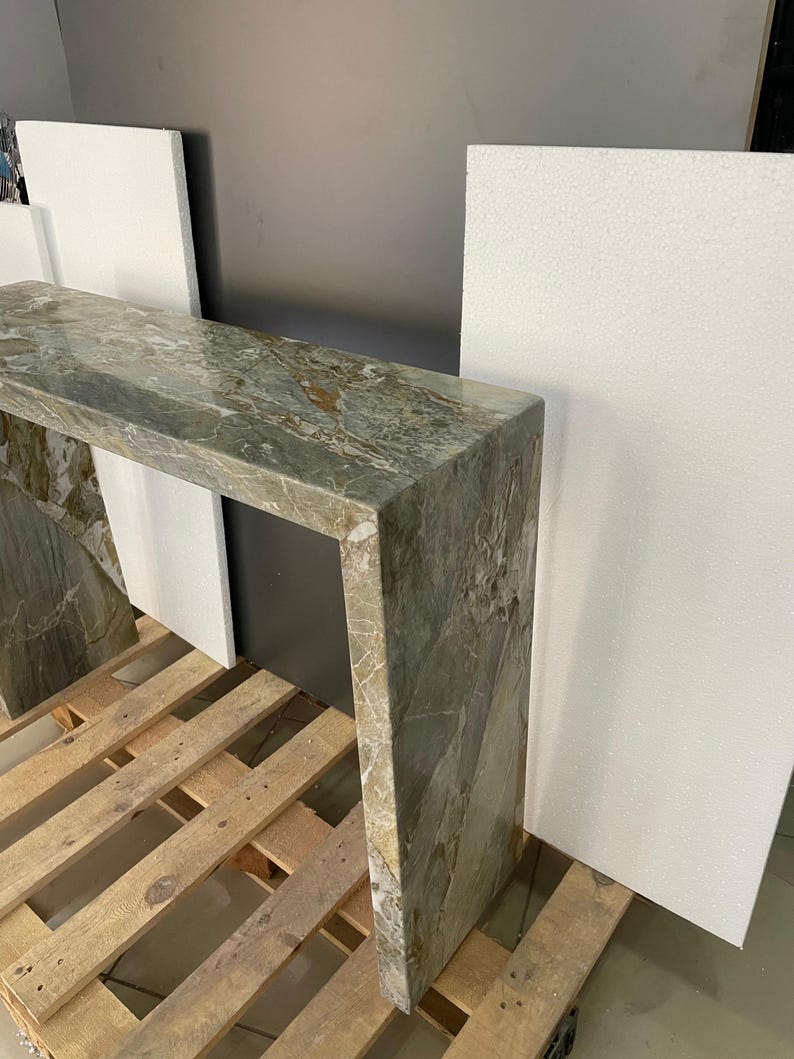 Pu&ograve; includere: Un tavolo console contemporaneo realizzato in marmo verde con un design asimmetrico unico. Il tavolo &egrave; sostenuto da un'unica gamba spessa su ogni lato, creando un look moderno e minimalista.
