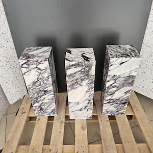 May include: Three white marble pedestals with purple veining. The pedestals are arranged in a row on a wooden pallet.