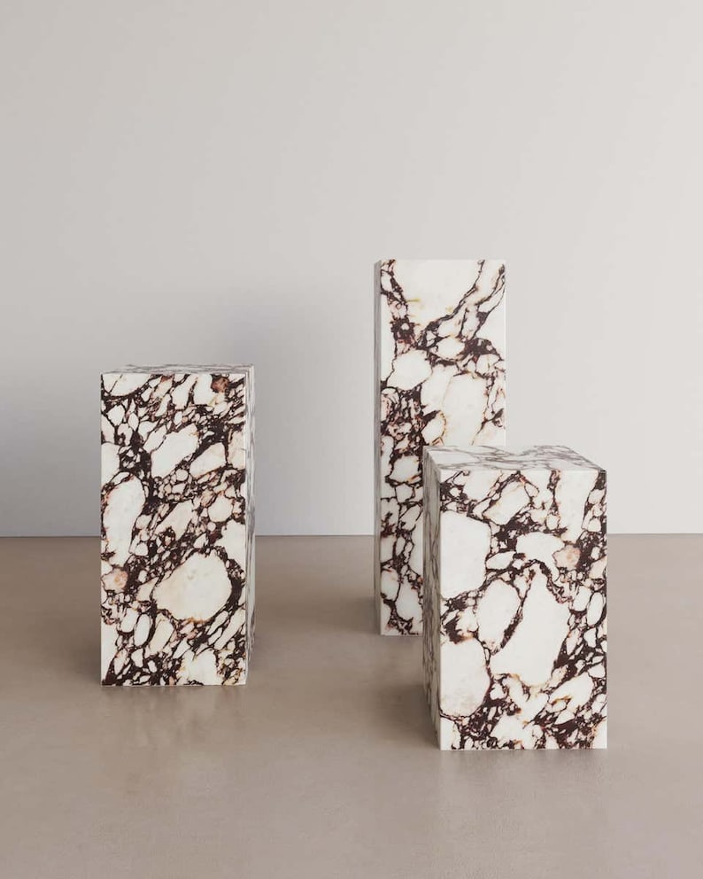 May include: Three white marble pedestals with brown veining. The pedestals are different sizes and are arranged in a row.