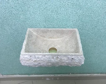 May include: A white ceramic sink with a rough, textured exterior is mounted on a light blue wall. The sink has a round drain hole in the center.