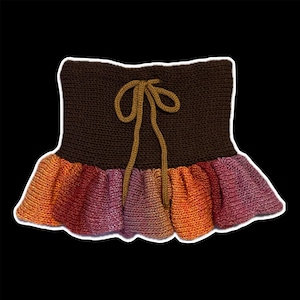 May include: A hand-knitted garment featuring a brown top and a ruffled skirt in shades of orange, red, and purple. A tan tie is centered on the front. The item is likely a top or a skirt.