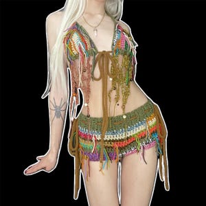 May include: A two-piece crochet set featuring a triangle halter top and matching shorts. The set is crafted from multicolored yarn in shades of olive green, orange, pink, and white, accented with dangling fringe, beads, and long tie-up straps.