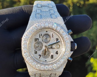 Può includere: Un orologio di lusso argentato, tempestato di numerose piccole gemme scintillanti. Il quadrante è chiaro, con più quadranti secondari e un datario. Il cinturino è abbinato. Lo sfondo è sfocato.