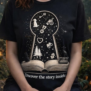 May include: Black t-shirt with a keyhole design containing illustrations of a dog, heart, and binoculars. The keyhole reveals a starry night sky. The text "Discover the story inside" is printed at the bottom of the design.