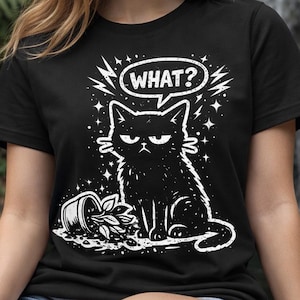 May include: Black t-shirt featuring a grumpy cat illustration with the word "WHAT?" in a speech bubble. The cat is sitting next to a tipped-over plant pot. The design is in white.