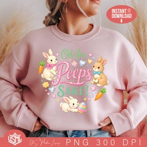 Może przedstawiać: Jasnoróżowa bluza z nadrukiem graficznym. Projekt przedstawia trzy króliki, marchewki i napis "Oh for Peeps Sake!". Projekt wykorzystuje pastelowe kolory i elementy dekoracyjne, idealne na Wielkanoc.