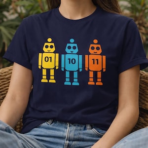 Könnte beinhalten: Marineblaues T-Shirt mit drei bunten Roboter-Illustrationen. Die Roboter sind gelb, blau und orange, jeder mit einer anderen Nummer: 01, 10 und 11. Das Design ist einfach und grafisch.