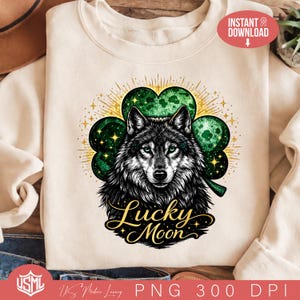 May include: Cream-colored sweatshirt featuring a detailed illustration of a wolf with green eyes, set against a green shamrock. The words "Lucky Moon" are written in gold script below the wolf. The design includes gold starburst accents.