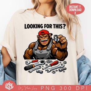 Puede incluir: Camiseta beige con el texto "LOOKING FOR THIS?" y un gorila de dibujos animados con una gorra roja y sosteniendo una llave de vaso. Varias herramientas se muestran debajo.