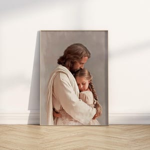 May include: A framed print shows a close embrace. A figure in white robes holds a young girl with braided hair. The artwork uses soft colours and a serene expression, creating a sense of comfort and peace.