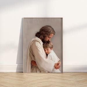 May include: A framed print depicts a tender embrace. A figure in white robes gently holds a young child, both with their eyes closed. The artwork is set against a soft, neutral background, creating a serene and comforting scene.
