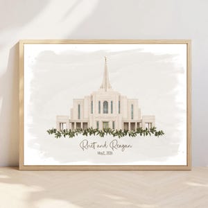 May include: A framed watercolor print featuring a light-colored temple with a central spire, accented by a green leafy garland at the base. Below the temple, the text reads Rhett and Reagan and the date May 2, 2026, in a dark script font.