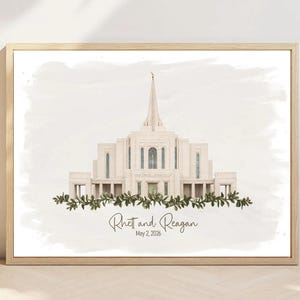 May include: A framed watercolor print featuring a beige temple with a central spire, accented by a green leafy garland at the base. The text reads Rhett and Reagan and May 2, 2026 in a dark script font centered below the architectural illustration.