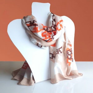 May include: A white scarf with a geometric pattern in orange and brown on a white mannequin.