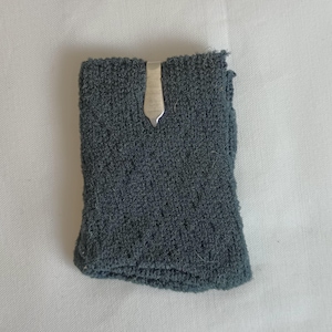 May include: A dark gray knitted sock with a silver metal clip attached to the top.