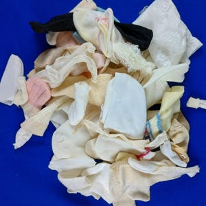 May include: A collection of various socks and undergarments in shades of white, cream, and pastel colors. Some items feature lace or decorative details. The items are arranged on a solid blue background.