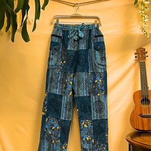 May include: Blue patchwork trousers with a drawstring waist and multiple pockets. The trousers feature a variety of patterns and designs, including paisley, stripes, and geometric shapes.
