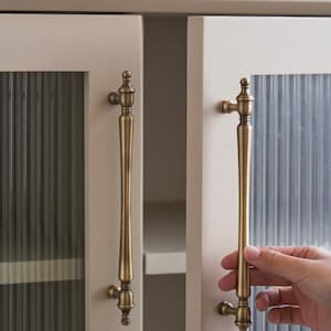 Puede incluir: Dos tiradores de puerta de armario de latón antiguo con un panel de vidrio acanalado detrás. El armario está pintado de un color crema claro.