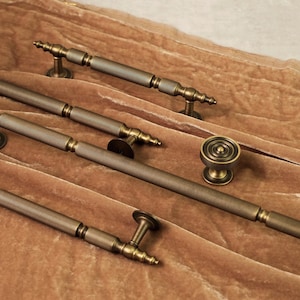 May include: A collection of antique brass cabinet hardware, including handles and a knob. The hardware features a ribbed design and a warm, aged finish. The pieces are arranged on a soft, brown velvet surface.