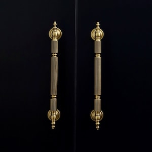 May include: Two gold door handles with a fluted design and a decorative finial on a black door.