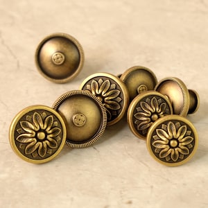 May include: A collection of antique brass cabinet knobs. The knobs have a round shape with a floral design in the center and a decorative edge. The brass finish gives them a vintage look.