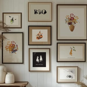 Puede incluir: Una galería de pared con impresiones artísticas enmarcadas con temática de Halloween. Las impresiones incluyen arte de huellas de manos de una bruja, un pavo, una calabaza, flores, fantasmas, una araña y la palabra "BOO". Los marcos son de color marrón oscuro.